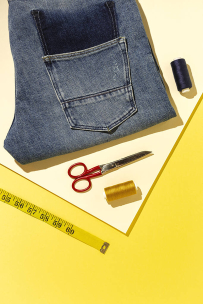 Handicraft, clothing repair. Ripped blue jeans sewing accessories with colorful background from above. Flat lay - Valokuva, kuva