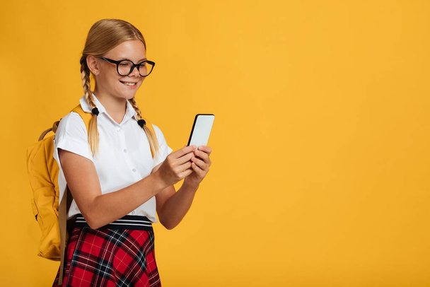 Lächelndes kaukasisches Teenie-Schulmädchen mit Zöpfen in Brille tippt auf Smartphone, plaudert bei Gadget - Foto, Bild