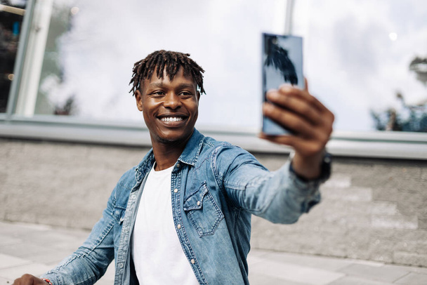 African American man takes a selfie on the street, in front of a glass building, traveling alone, a photo for memory - Foto, Imagem