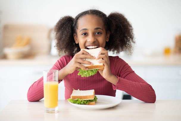 Μια όμορφη μαύρη έφηβη τρώει σνακ στο σπίτι. - Φωτογραφία, εικόνα