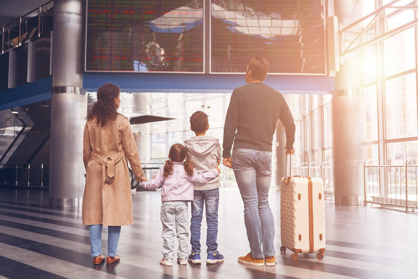Rear view of family with two little kids looking at the flight information board - Foto, Bild