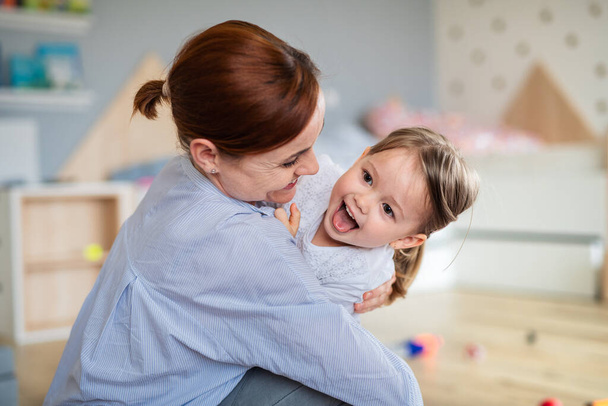 Happy mother with small daughter playing indoors in bedroom, laughing. - Foto, imagen