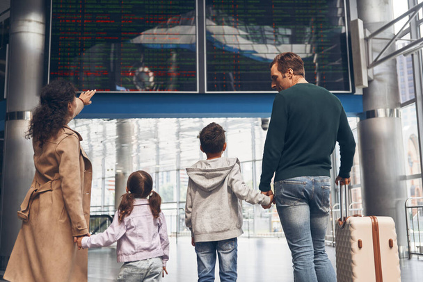 Rear view of family with two little kids looking at the flight information board - Fotografie, Obrázek