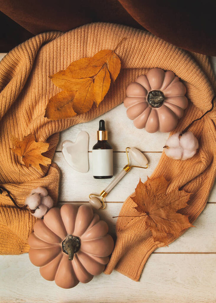 Productos para el cuidado de la piel en otoño: botella de cosméticos, masajeador de jade, guasha, hojas de otoño, calabazas, suéter de punto. Rutina de belleza estacional y concepto de cuidado orgánico de la piel. - Foto, imagen