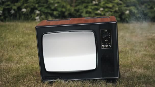 Old vintage retro TV stands on the grass. Smoke billows from the damaged device - Footage, Video