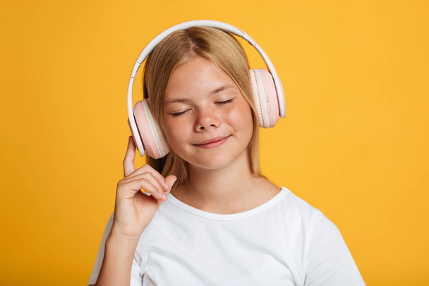 Retrato de calma bonito adolescente europeu feminino em t-shirt branca com olhos fechados em fones de ouvido sem fio ouvir música - Foto, Imagem