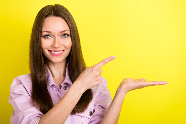 Portrait of attractive confident cheerful girl holding on palm demonstrating copy space ad isolated over bright yellow color background - Foto, imagen