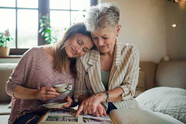 Front view of senior mother with adult daughter indoors at home, looking at family photographs. - Foto, Imagen