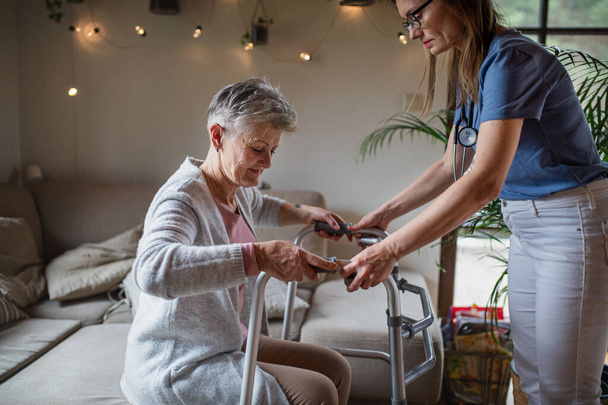 Egészségügyi dolgozó vagy gondozó látogató idősebb nő otthon, segít neki járni. - Fotó, kép