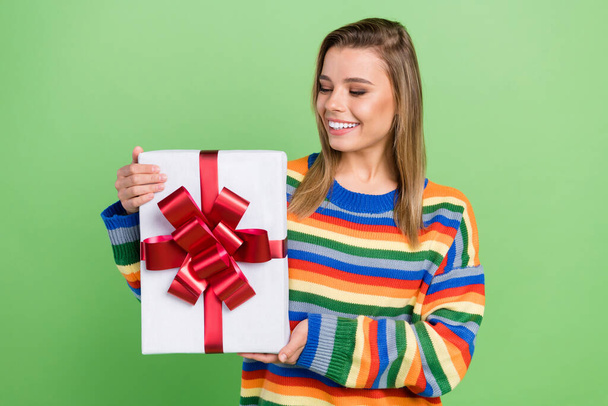 Photo portrait girl keeping gift box smiling at birthday party enjoying in striped sweater isolated pastel green color background - Foto, immagini