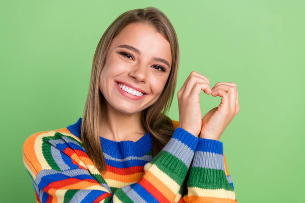 Photo portrait girl smiling showing heart sign on date in striped sweater isolated pastel green color background - Zdjęcie, obraz