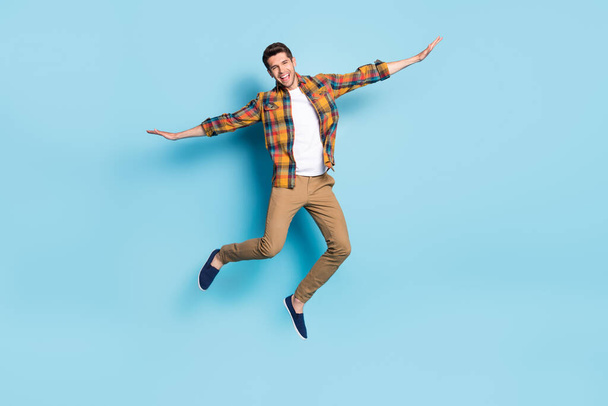 Photo of funny pretty young guy dressed plaid shirt spectacles smiling jumping high isolated blue color background - Fotó, kép