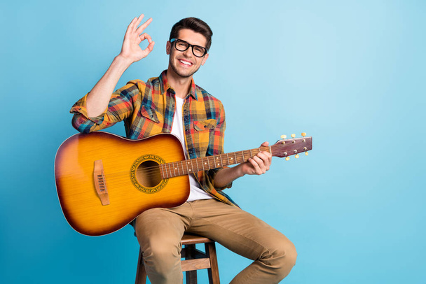 Photo of dreamy attractive gentleman wear checkered shirt holding guitar showing okey empty space isolated blue color background - Photo, image