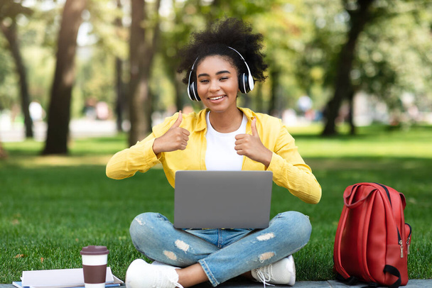 Чорна дівчина з ноутбуком жестикулює великими пальцями вгору з обома руками зовні
 - Фото, зображення