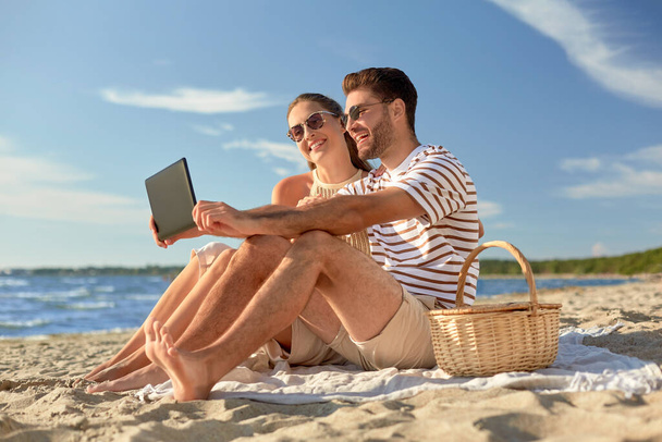 happy couple with tablet pc at picnic on beach - Zdjęcie, obraz