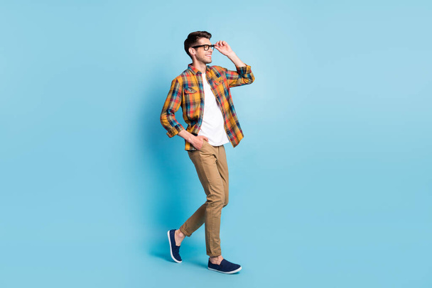Photo of cute charming young guy dressed plaid shirt spectacles smiling walking looking empty space isolated blue color background - Valokuva, kuva
