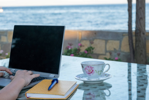 Woman working seaside on laptop and drink coffee, remote professional work life in holiday, home office - Photo, Image