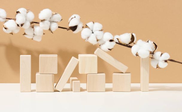 drewniane kostki ułożone i gałęzie z białymi kwiatami bawełny na brązowym tle. Podium dla produktów kosmetycznych, napojów i żywności, produktów ekologicznych - Zdjęcie, obraz