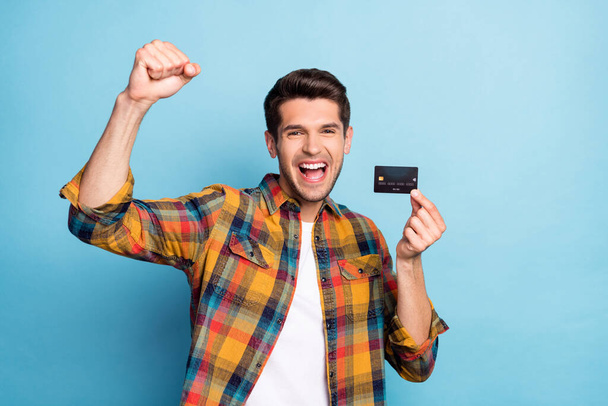 Portrait of attractive cheerful guy holding in hand bank card celebrating having fun deposit isolated over bright blue color background - Photo, Image