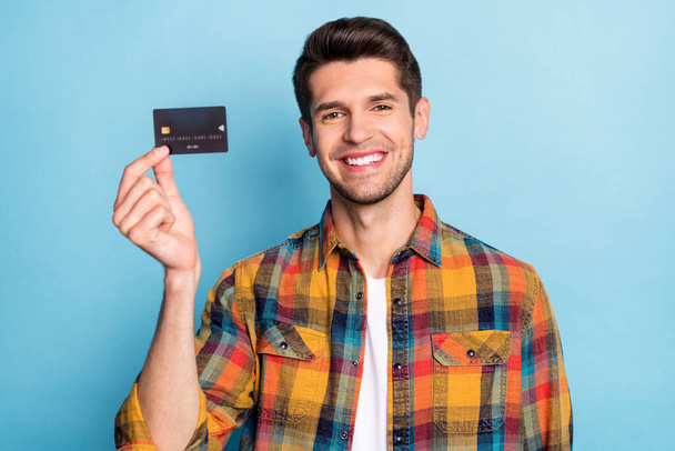 Portrait of attractive cheerful guy holding in hand black bank card savings deposit isolated over bright blue color background - Fotografie, Obrázek