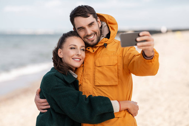 couple with smartphone on autumn beach - Foto, afbeelding