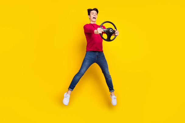 Full length photo of cute shocked young guy dressed red pullover driving car jumping isolated yellow color background - Foto, afbeelding