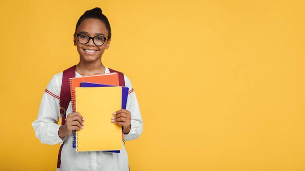 Smiling smart teenage afro american female pupil in glasses with backpack hold many books, notebooks, looking at camera - Foto, imagen