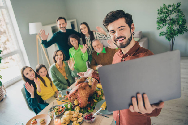 Foto de adorable divertida familia celebrando gracias dando día sentado mesa hablando dispositivo moderno sonriendo en el interior habitación casa - Foto, imagen