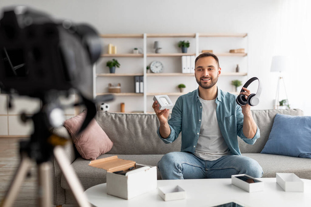 Young male influencer recording video review, comparing new wireless headphones and earphones models at home - Foto, imagen