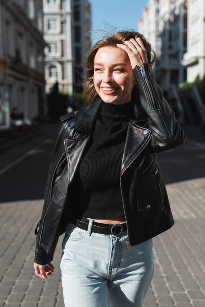 felice giovane donna in giacca di pelle in piedi sulla strada urbana  - Foto, immagini