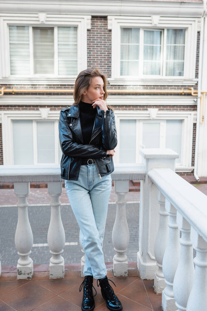 ヨーロッパの都会の通りに立つ黒い革のジャケットを着た若い女性が  - 写真・画像