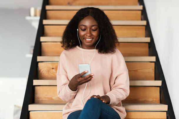 gelukkig zwart vrouw luisteren naar muziek op telefoon thuis - Foto, afbeelding