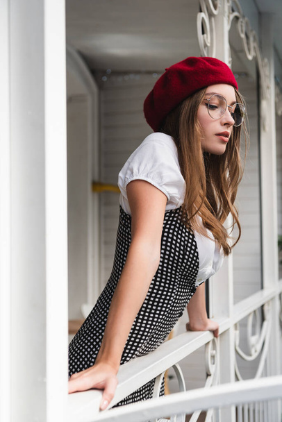 pretty young woman in red beret and eyeglasses standing on balcony - Foto, Imagem