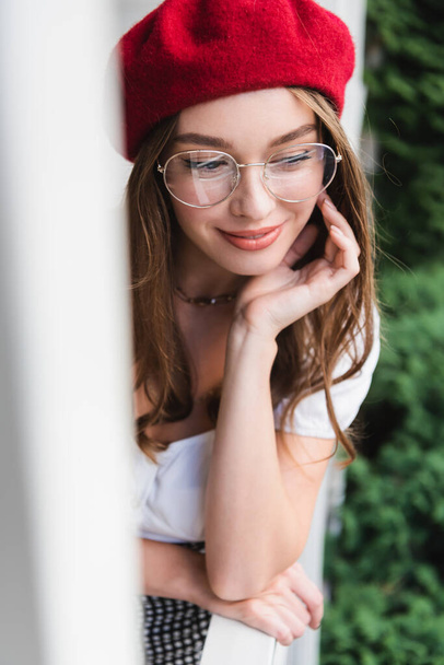 pleased young woman in red beret and eyeglasses looking away outside - Foto, imagen