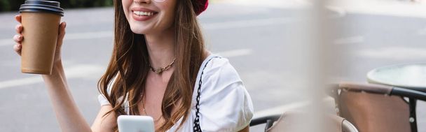 cropped view of cheerful woman holding paper cup and smartphone, banner - Photo, Image