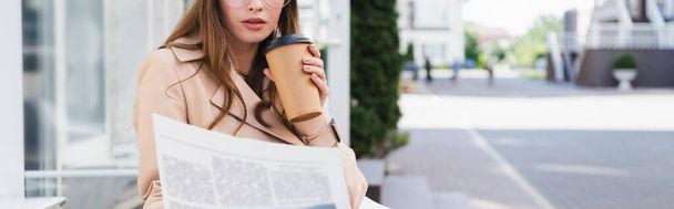 обрізаний вид молодої жінки в траншеї пальто тримає паперовий стаканчик під час читання газети, банер
  - Фото, зображення