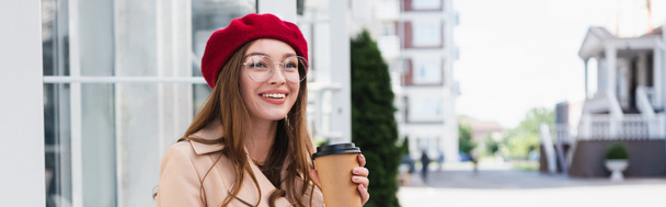 happy young woman in red beret and beige trench coat holding paper cup, banner - Fotoğraf, Görsel