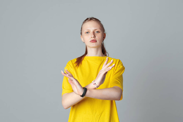 Serious teen girl making X sign with her arms to stop doing something, isolated on light grey background, wearing in casual blank yellow t shirt. Stop, no, stay back. Concept of warning, prohibition - Photo, Image
