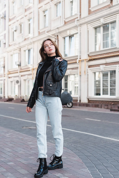 full length of stylish young woman in black turtleneck and leather jacket on urban street of europe  - Photo, Image