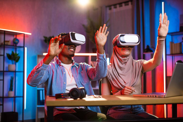 Young multiethnic couple playing games or working using VR goggles at home - Photo, image