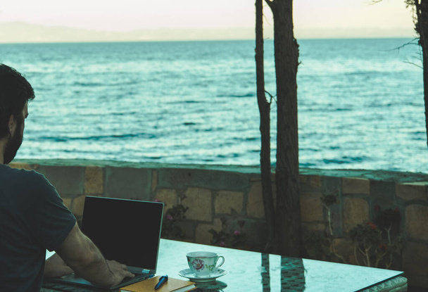 Konzept eines professionellen freiberuflichen Geschäftsmannes, der vom Laptop aus im Urlaub vom Ferienhaus aus arbeitet, Fernarbeit im Urlaub, Mobilität mit Technologie - Foto, Bild