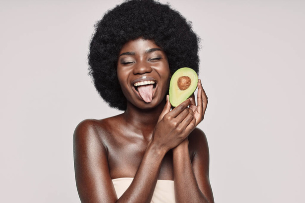 Portrait of beautiful young African woman holding avocado and grimacing - Foto, Imagem