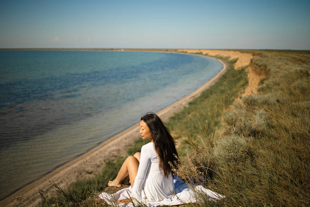 Asyalı bir kız okyanusa bakan bir kayanın üzerinde sessizce oturuyor. - Fotoğraf, Görsel
