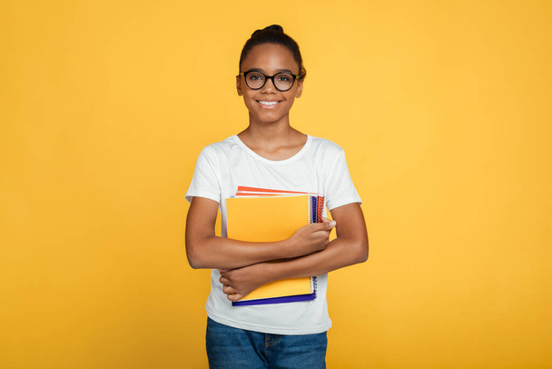 Cheerful teenage african american girl pupil in glasses and casual holds books and ready to learn - Foto, Imagem