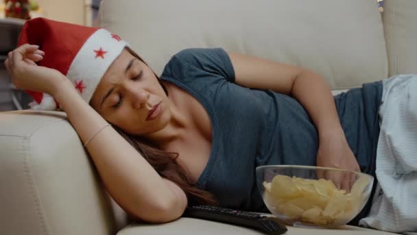 Persona assonnata con cappello da Babbo Natale e seduta alla TV con patatine fritte - Filmati, video