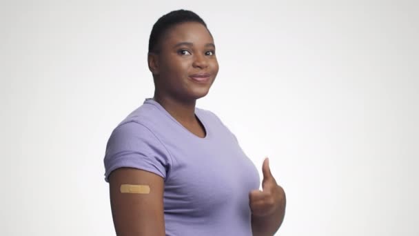 Fröhlich geimpfte Afroamerikanerin zeigt Schulter mit Gips nach Injektion und gestikulierendem Daumen nach oben - Filmmaterial, Video