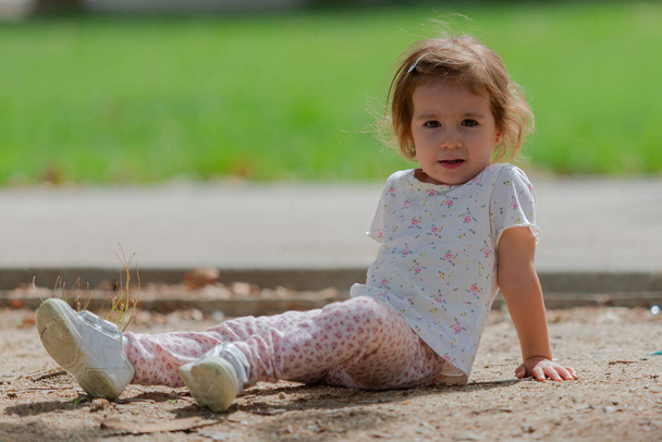 Tyttö istuu nurmikolla puistossa. Lapset ulkona - Valokuva, kuva