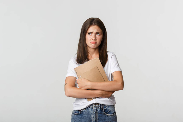 Retrato de triste y decepcionado estudiante linda mujer sosteniendo cuadernos y mirando esquina superior izquierda molesto - Foto, imagen