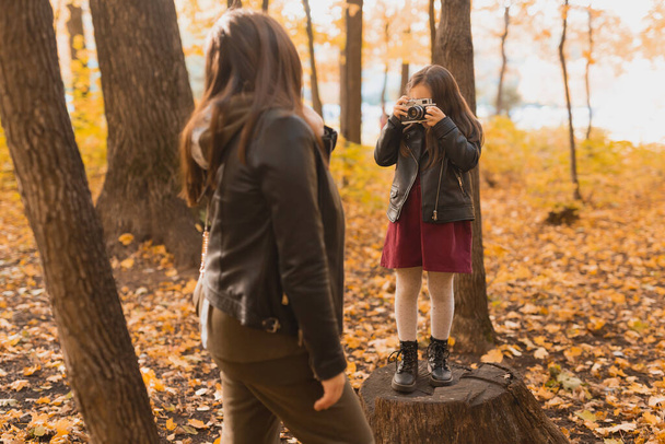 Niño tomando fotos de su madre en cámara retro en el parque de otoño. Hobbies y concepto de ocio. - Foto, Imagen