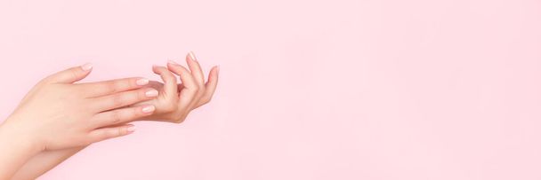 Female hands with beautiful manicure - pink nude nails on pink background, wide panoramic banner with copy space. Nail care concept - Photo, Image
